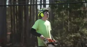 Webb Tree Services crew member in a hard hat, ear defenders and safety glasses holding a chainsaw on a Connecticut job
